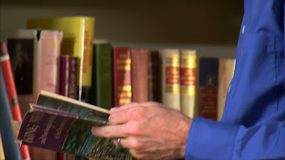 Books on a shelf. Person holding a book.